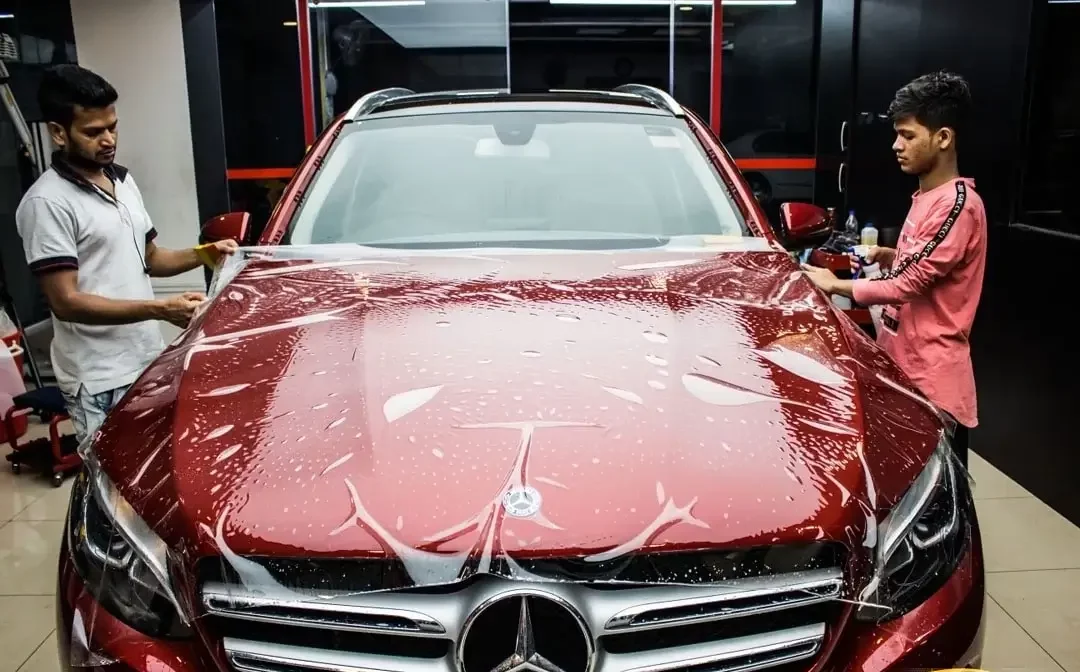 A maroon-coloured car’s hood being installed with paint protection film on it